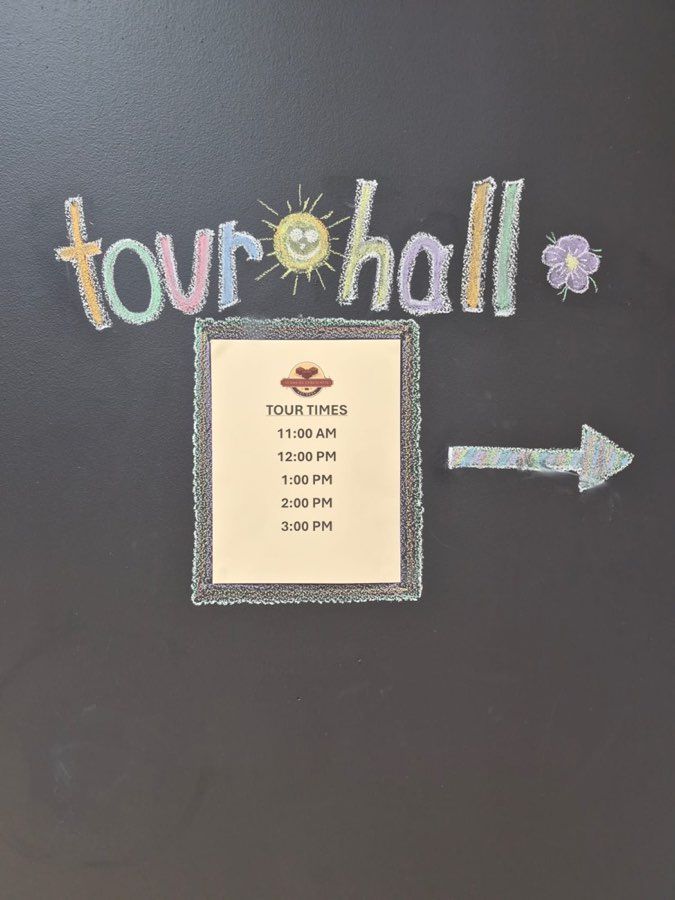 Chalkboard pointing to the tour hall with hourly tour times from 11 AM to 3 PM